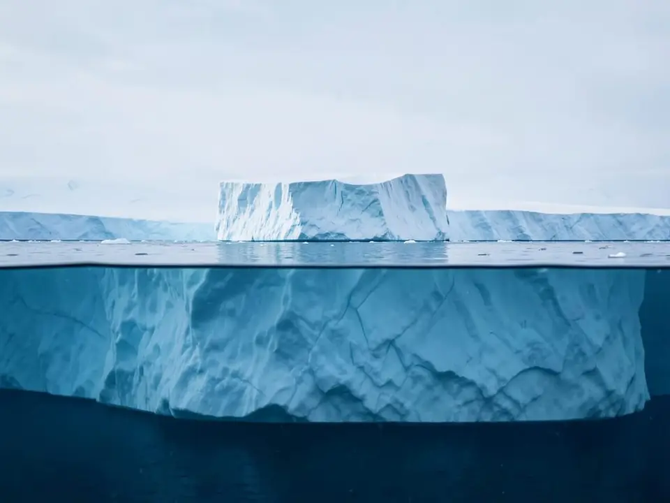 An iceberg at the waterline, its small visible peak above the surface and its far larger mass below, evoking a settlement described as just the tip of the iceberg. AI-generated editorial illustration; not a documentary photograph