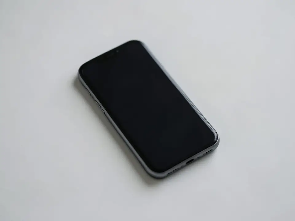 A single unbranded smartphone with a dark screen rests on a plain surface, representing a company that leads the smartphone market but trails rivals in AI. AI-generated editorial illustration; not a documentary photograph