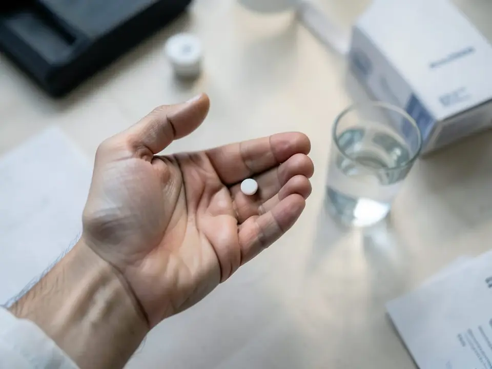 An anonymous adult's open hand holds a single small white pill beside a glass of water, representing the daily upadacitinib dose of a 15mg dose, a 30mg dose, or a placebo pill every day. AI-generated editorial illustration; not a documentary photograph