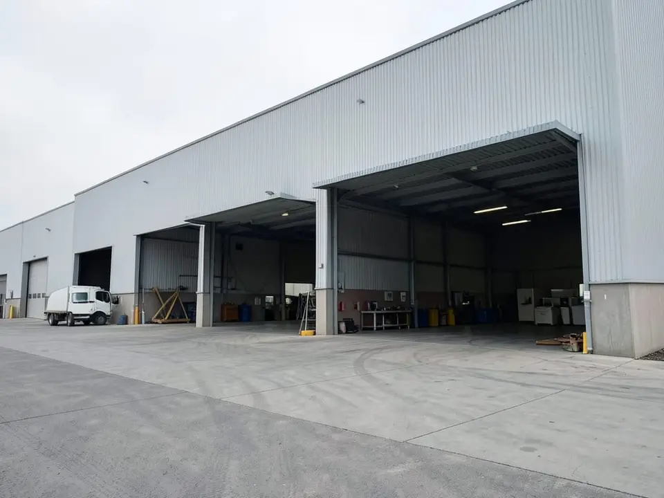 The wide exterior of a large industrial facility, the kind of larger facility the company chose after it mapped out employees' zip codes for more digestible commute times. AI-generated editorial illustration; not a documentary photograph