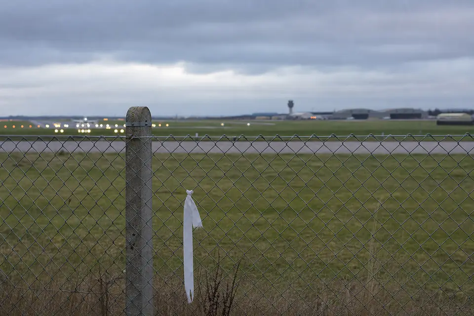 Anti-war activists have protested outside a UK airbase, shown gathered from behind with the airbase exterior in the background. AI-generated editorial illustration; not a documentary photograph