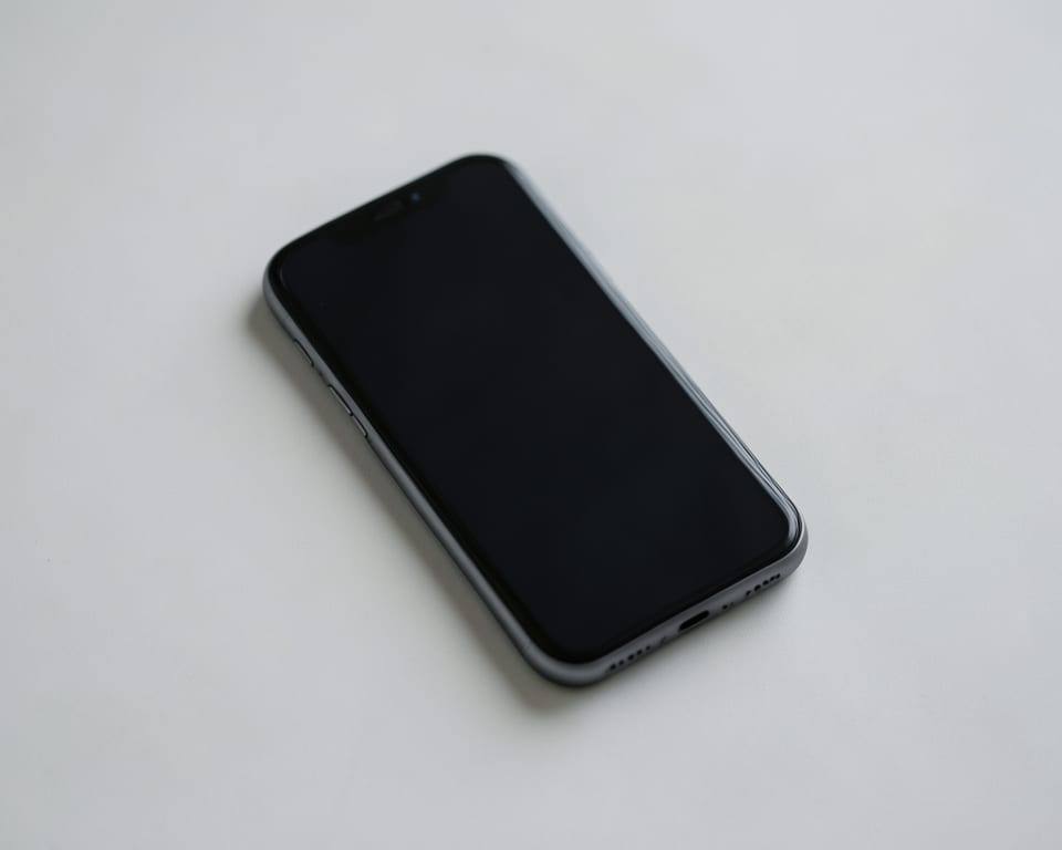 A single unbranded smartphone with a dark screen rests on a plain surface, representing a company that leads the smartphone market but trails rivals in AI. AI-generated editorial illustration; not a documentary photograph